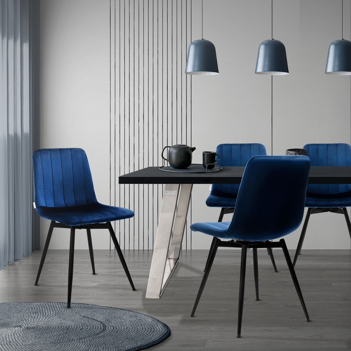 Eethoek met blauwe gestoffeerde stoelen, een zwarte tafel, een grijs vloerkleed en drie hanglampen.