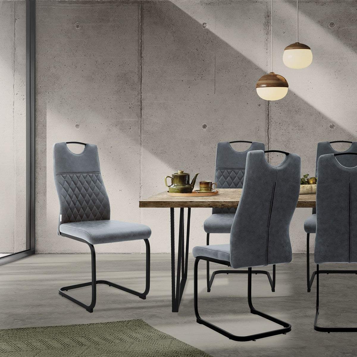 Graue Freischwingerstühle mit gesteppten Rückenlehnen stehen an einem Holztisch in einem Raum mit Betonwand.