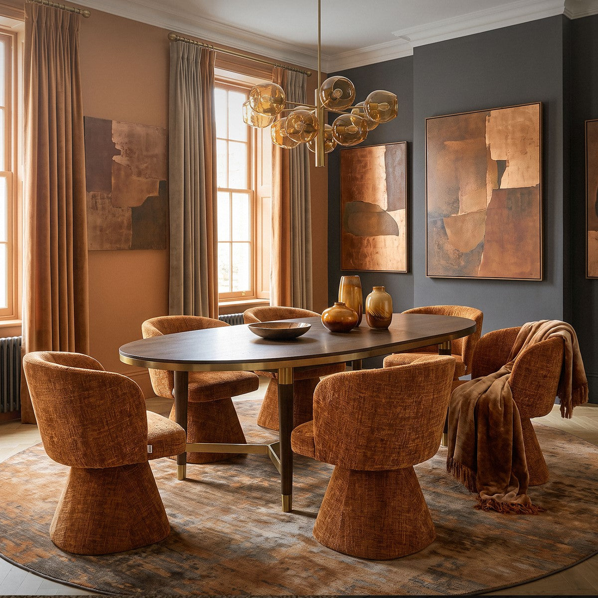 Esszimmer mit ovalem dunklem Tisch, braunen Polsterstühlen, abstrakten Wandbildern und goldener Pendelleuchte.