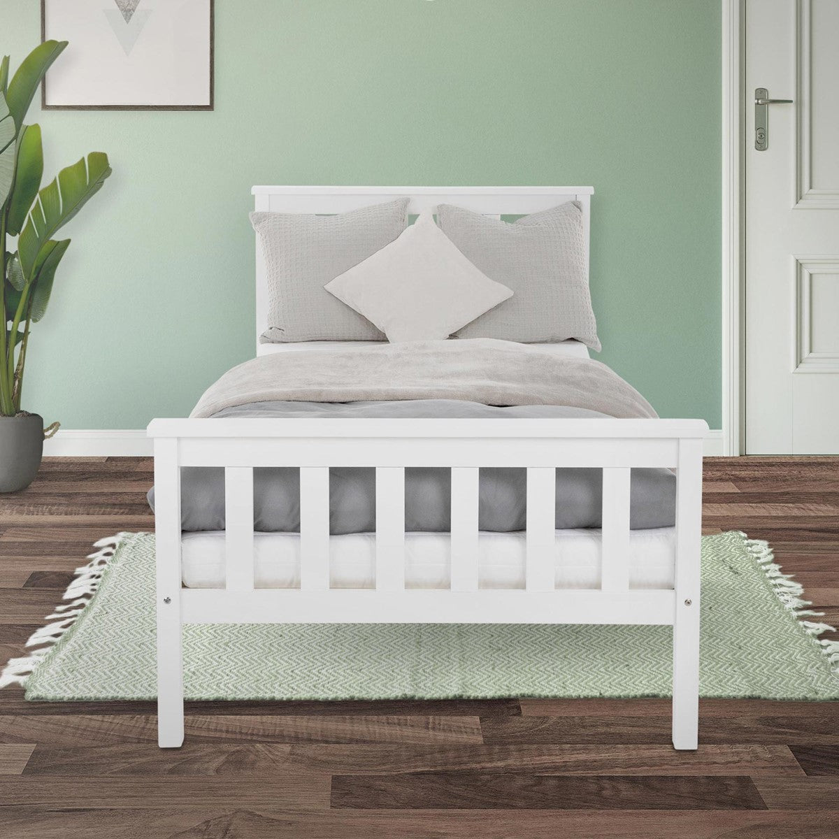 Bílá postel s šedým ložním prádlem a polštáři před zelenou stěnou.