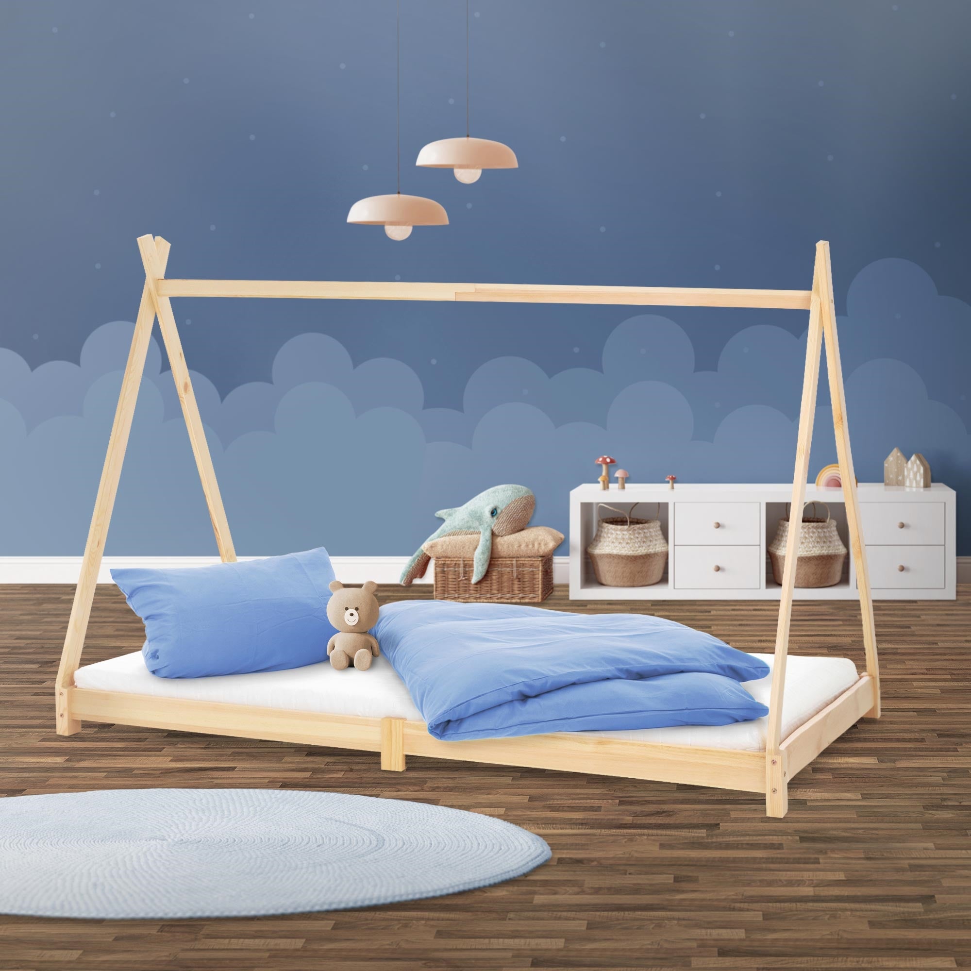 Bett im Kinderzimmer mit blauen Kissen und Decke, Holzrahmen und Wand mit Wolkenmuster.