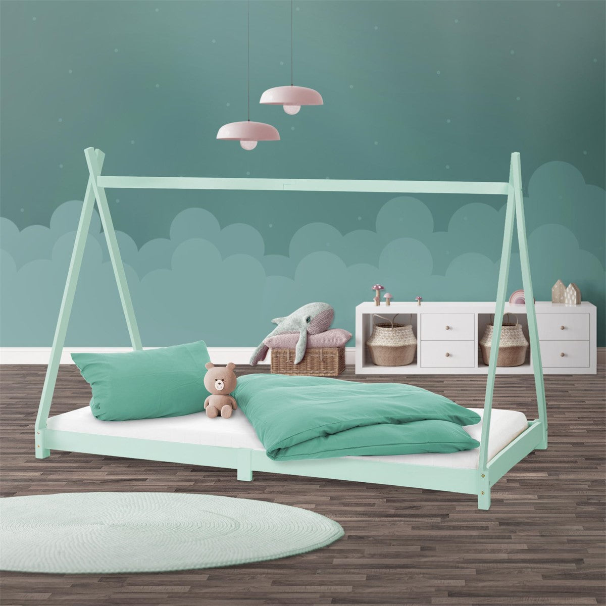 Mint-green cot with a house-shaped frame, green bedding and soft toys in front of a turquoise wall.