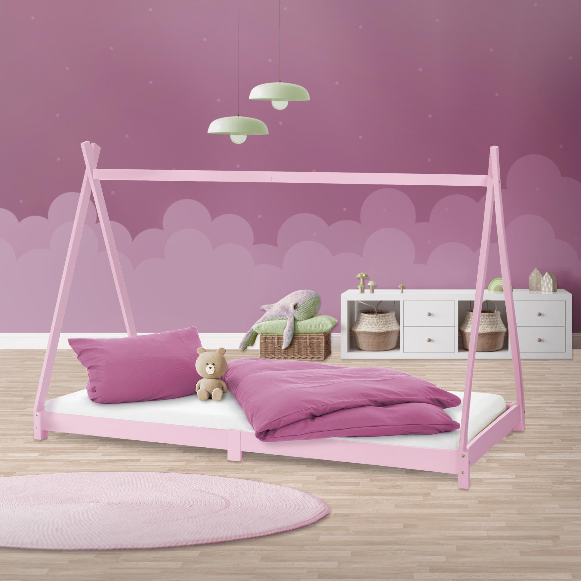 Rosa Kinderbett mit Kissen und Decke vor einer lila Wand.