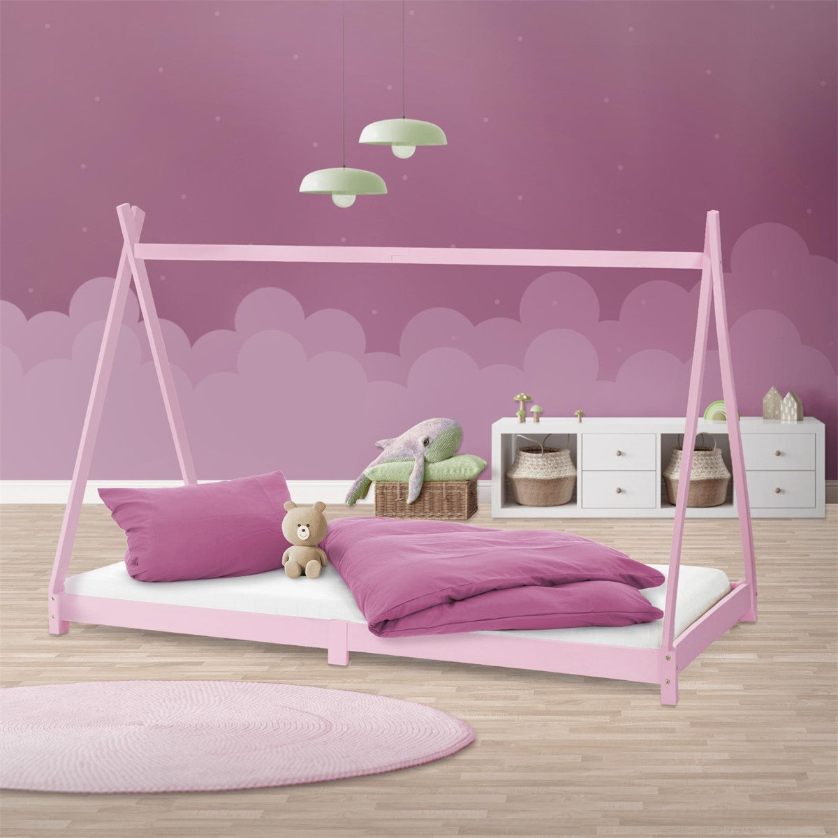 Cama casinha rosa com roupa de cama cor-de-rosa, uma almofada e um urso de peluche diante de uma parede roxa.