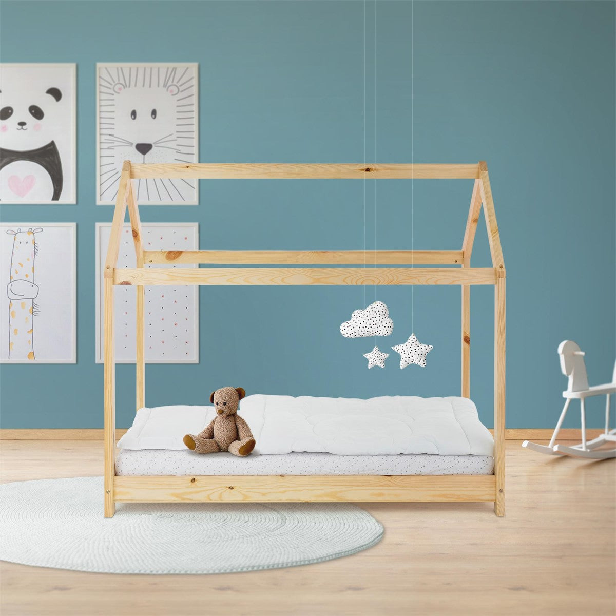 Helles Holzbett mit offenem Hausgestell und Teddybär, vor einer blauen Wand mit gerahmten Tierbildern.