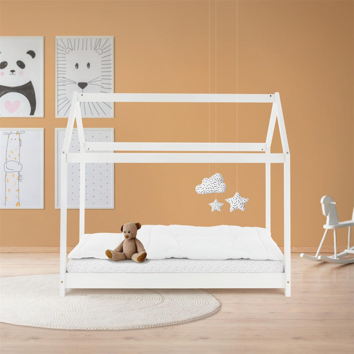 Weißes Kinderbett mit hausförmigem Gestell, weißer Bettwäsche und Teddybär in einem beigefarbenen Kinderzimmer.