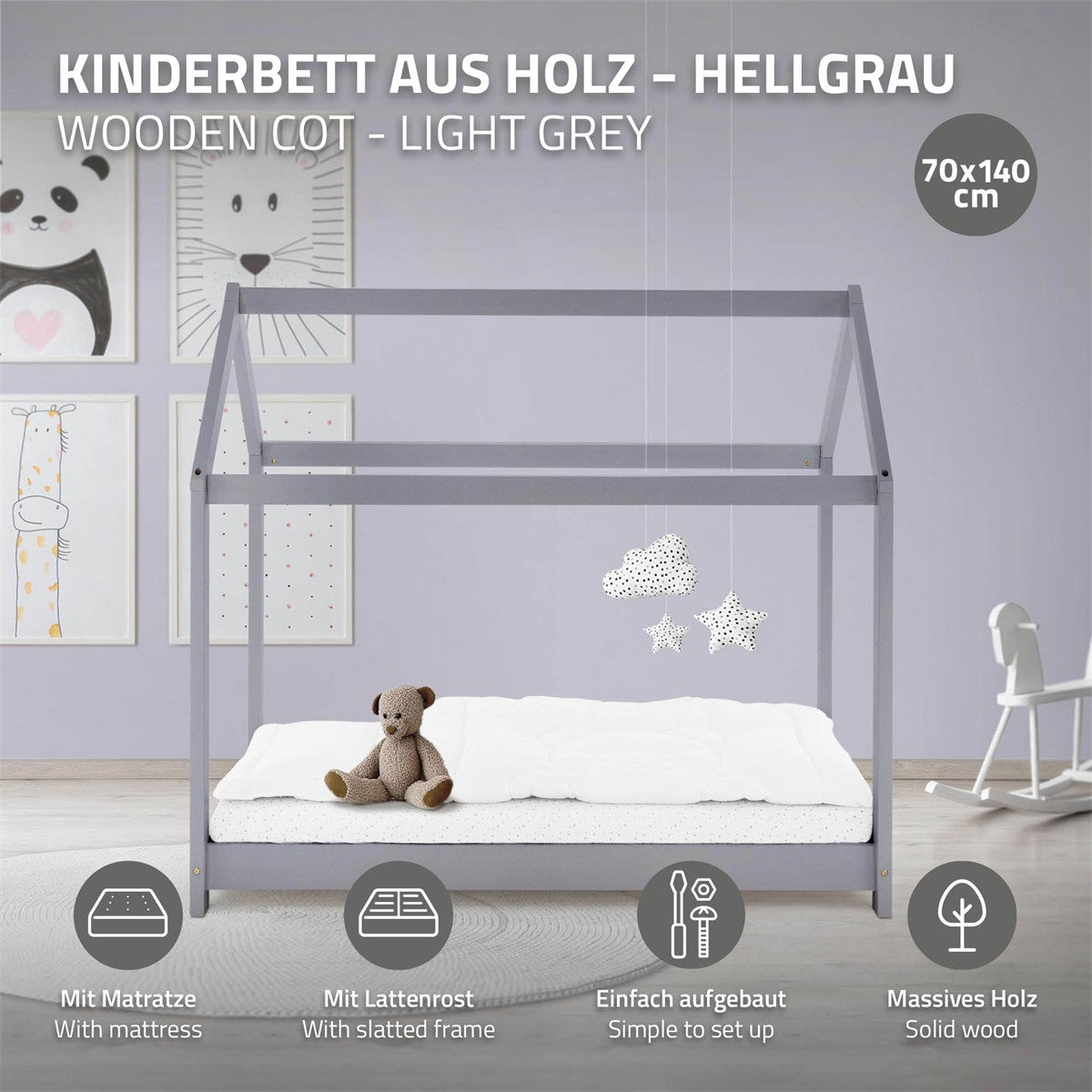 Hellgraues Holz-Kinderbett mit Matratze, an einer Wand mit Bildern.