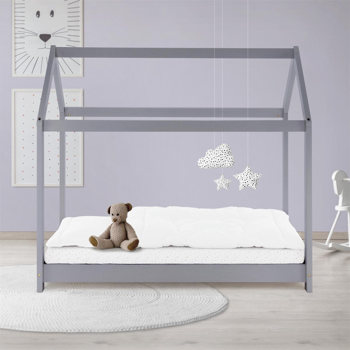 Holzgestell in Hausform mit Teddy auf einer Matratze in einem Kinderzimmer.
