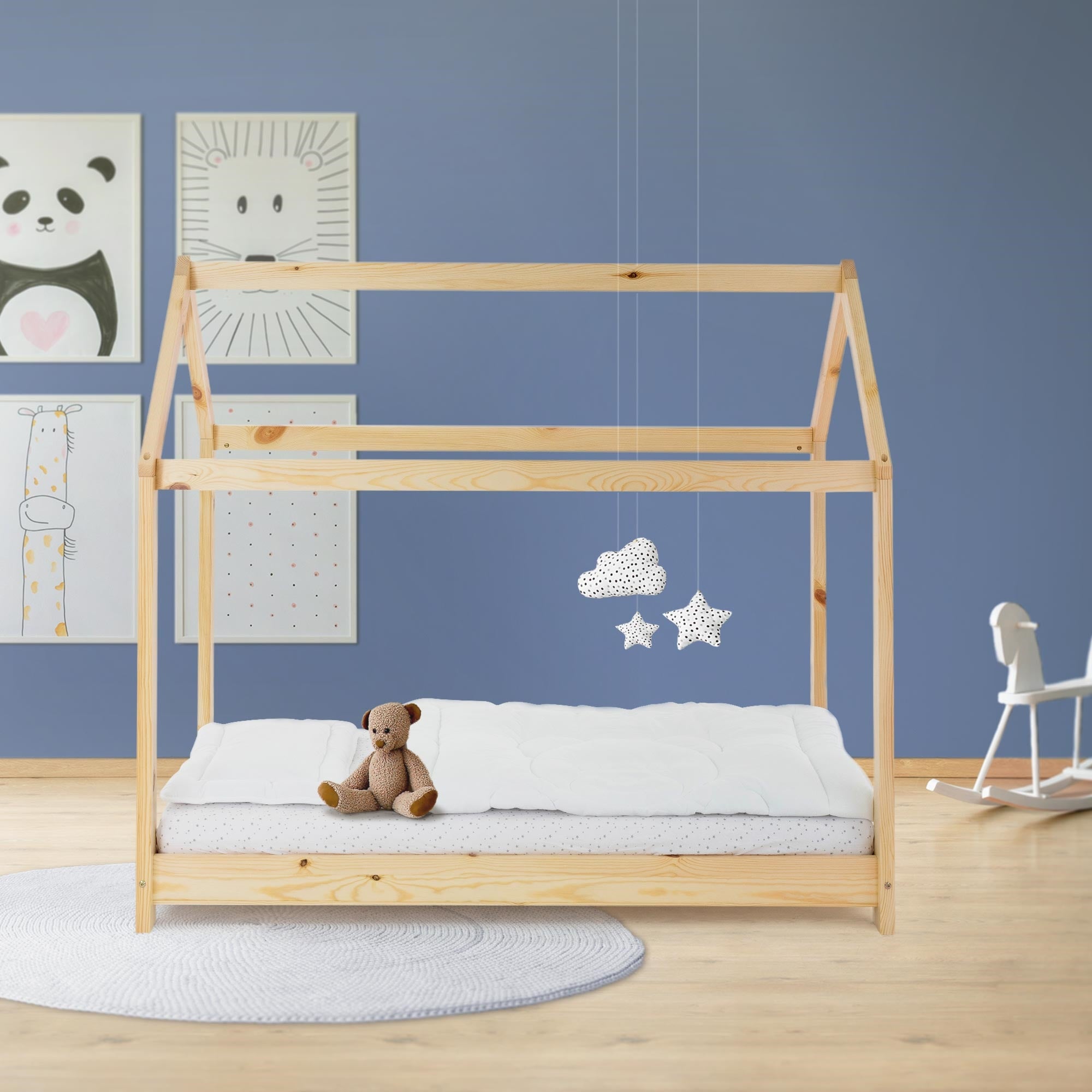 Holz-Kinderbett mit Teddy und Wolken, an einer blauen Wand mit Bildern.