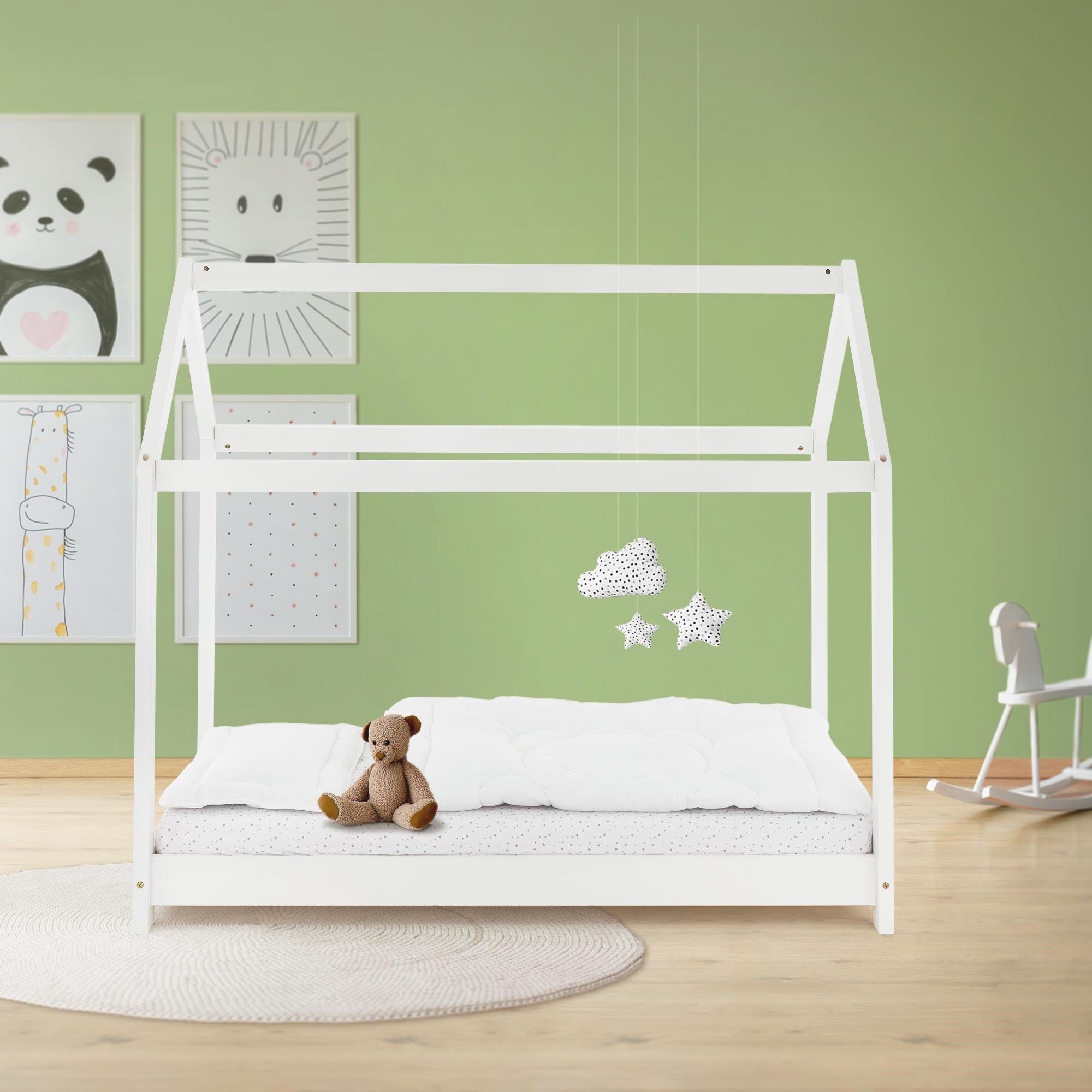 Ein weißes Kinderbett mit Matratze und Teddybär in einem grünen Raum.