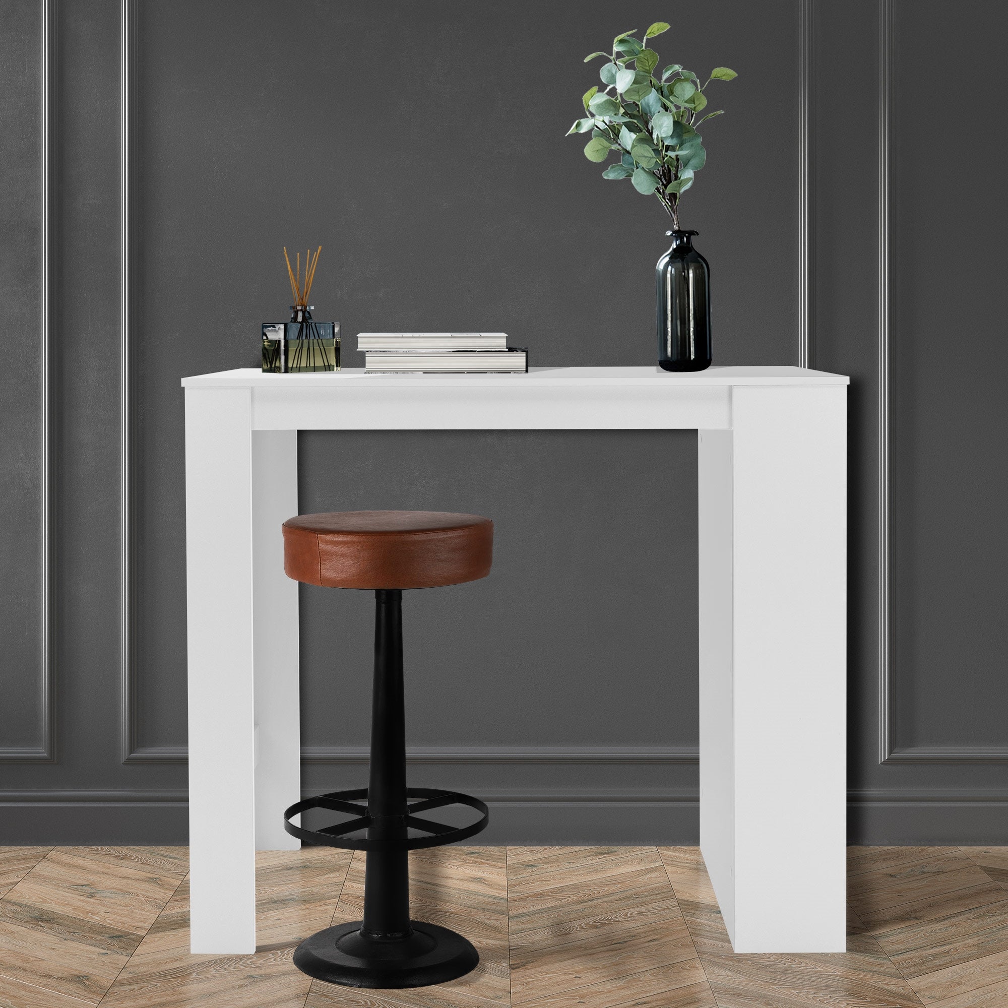 Weißer Tisch mit einem Hocker, Pflanze und Bücher auf der Tischplatte.