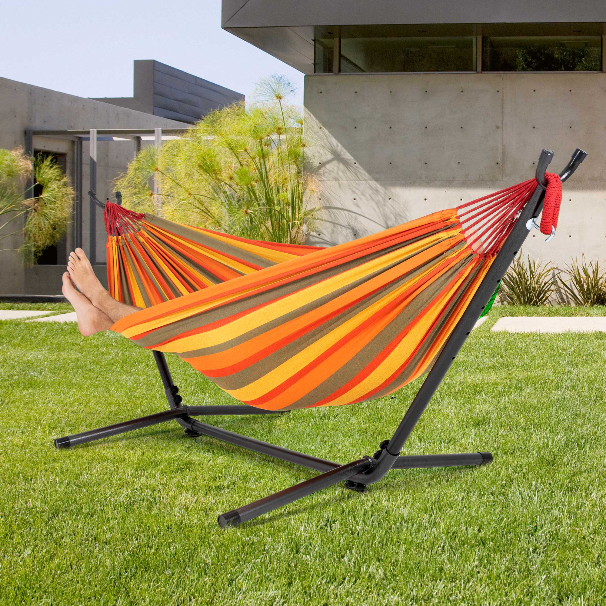 Colorful hammock on a lawn with feet visible.