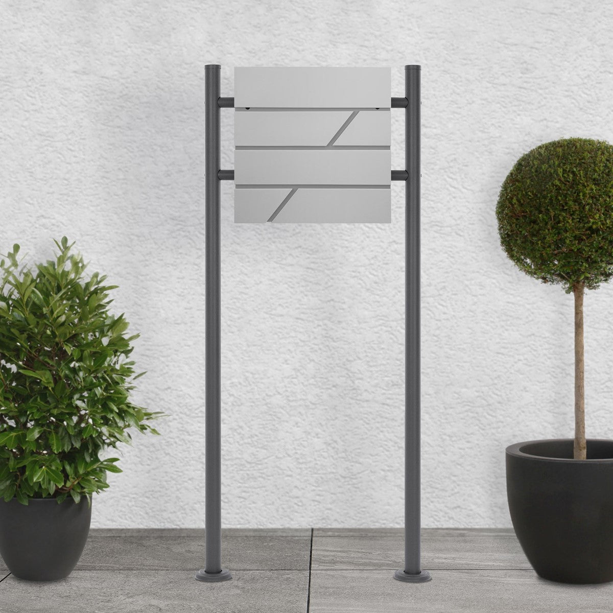 Letterbox on a stand between two round plants in pots.