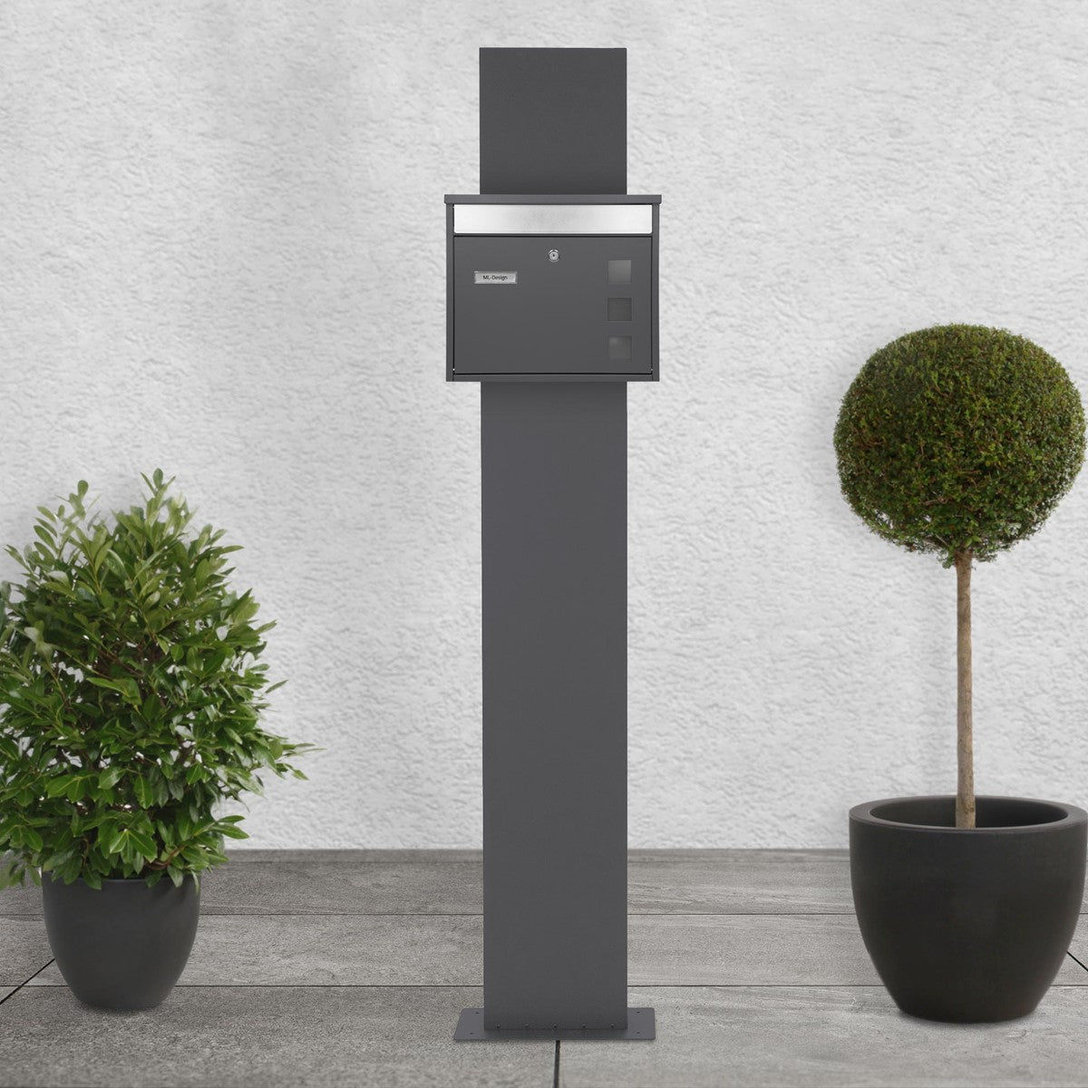 Mailbox on a stand, surrounded by two round plants.