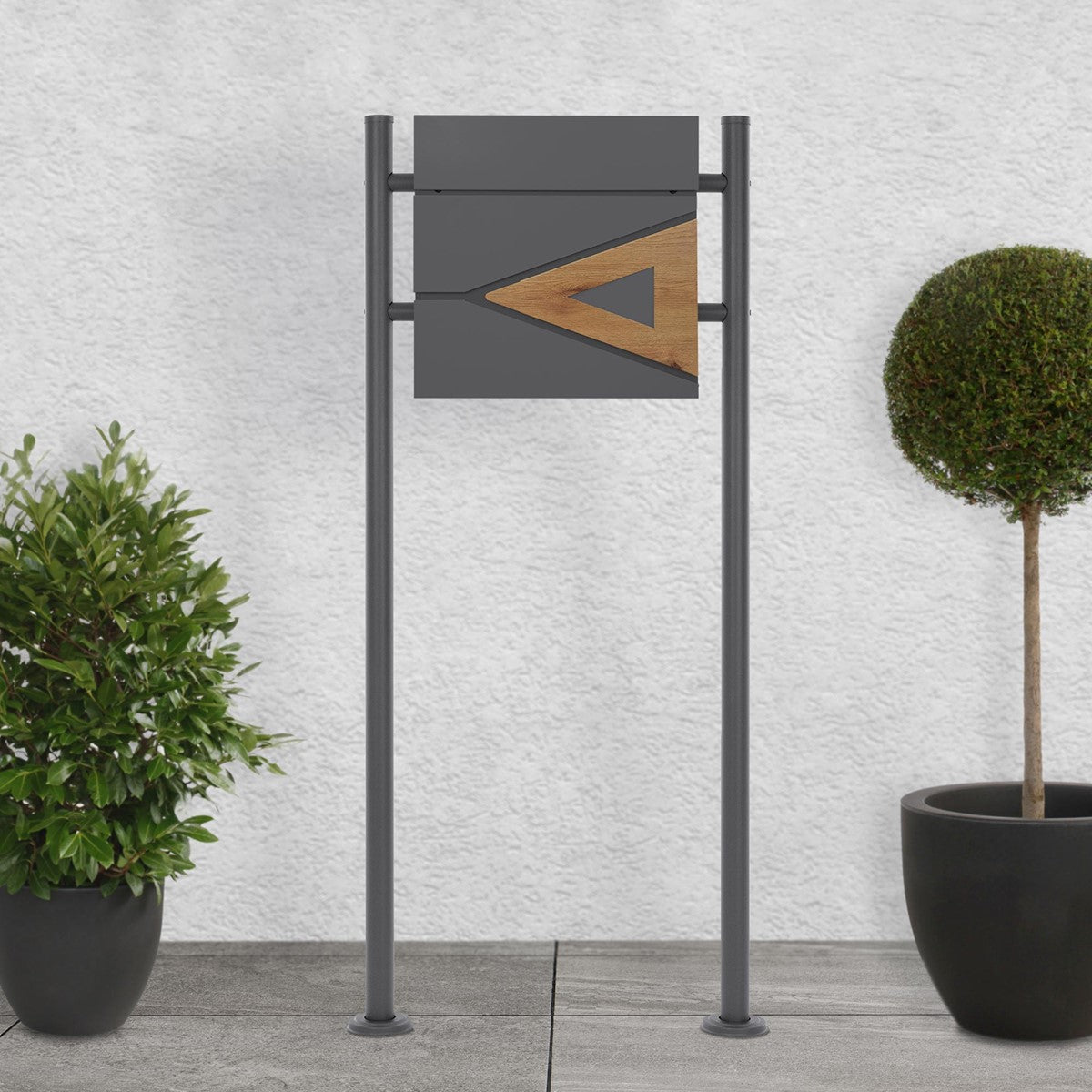 Mailbox with a wooden element, surrounded by two plants on a grey floor.