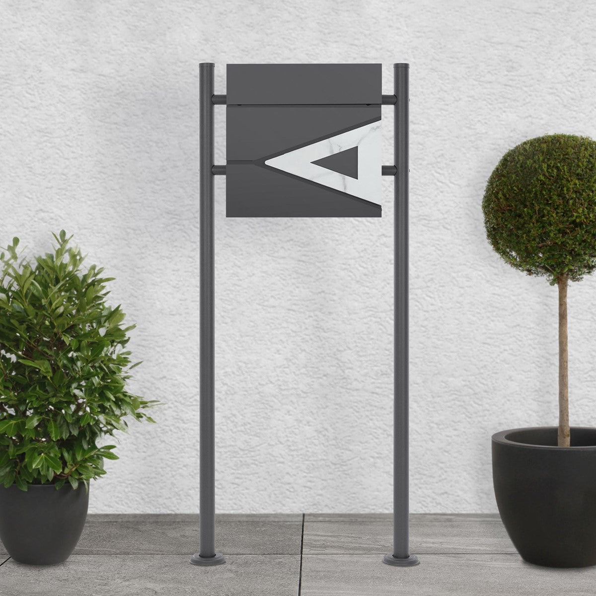 Boîte aux lettres entre deux plantes sur un trottoir.