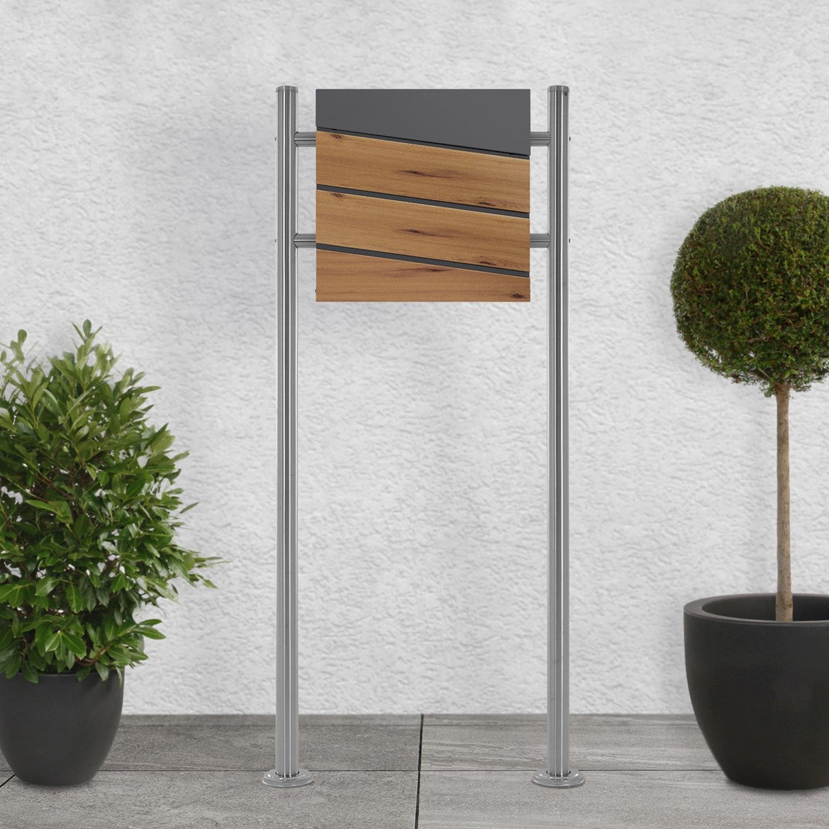 Mailbox with a wooden front, on two supports, surrounded by plants.