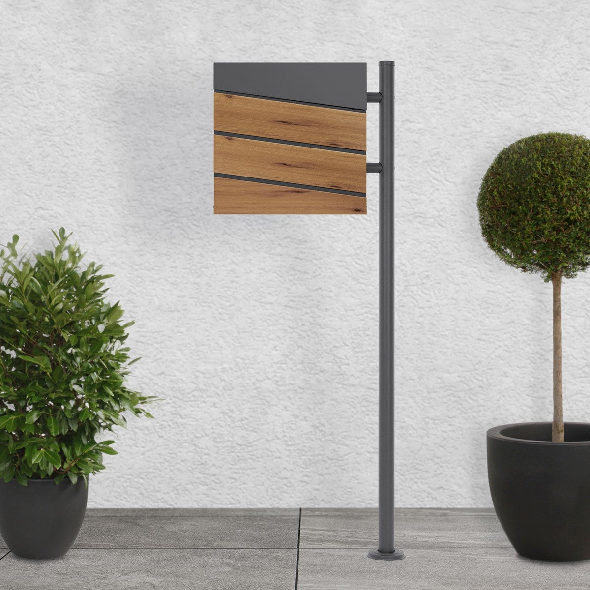 Mailbox with a wooden front and gray frame, surrounded by two plants.