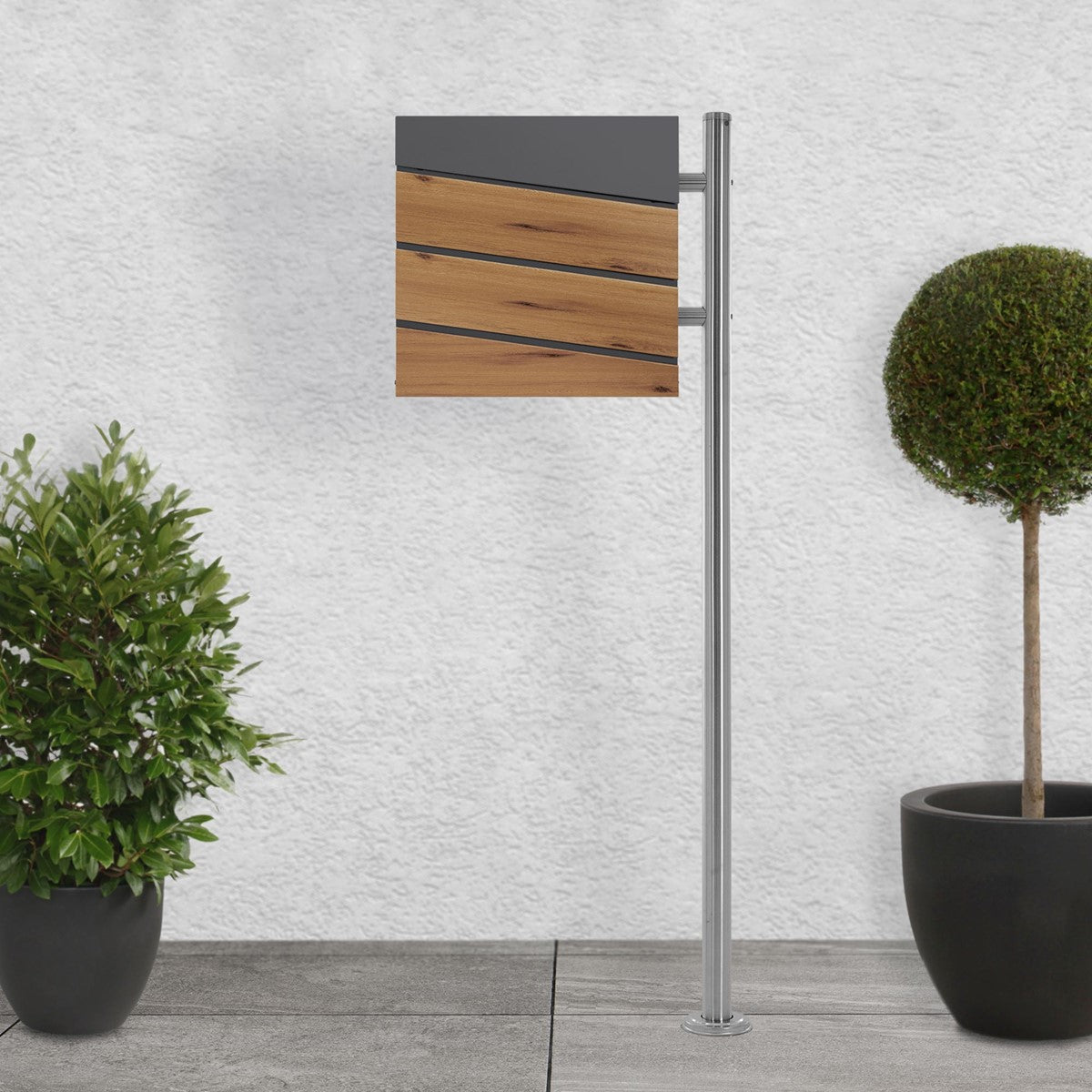 Mailbox in anthracite with oak decor, on a walkway beside plants.