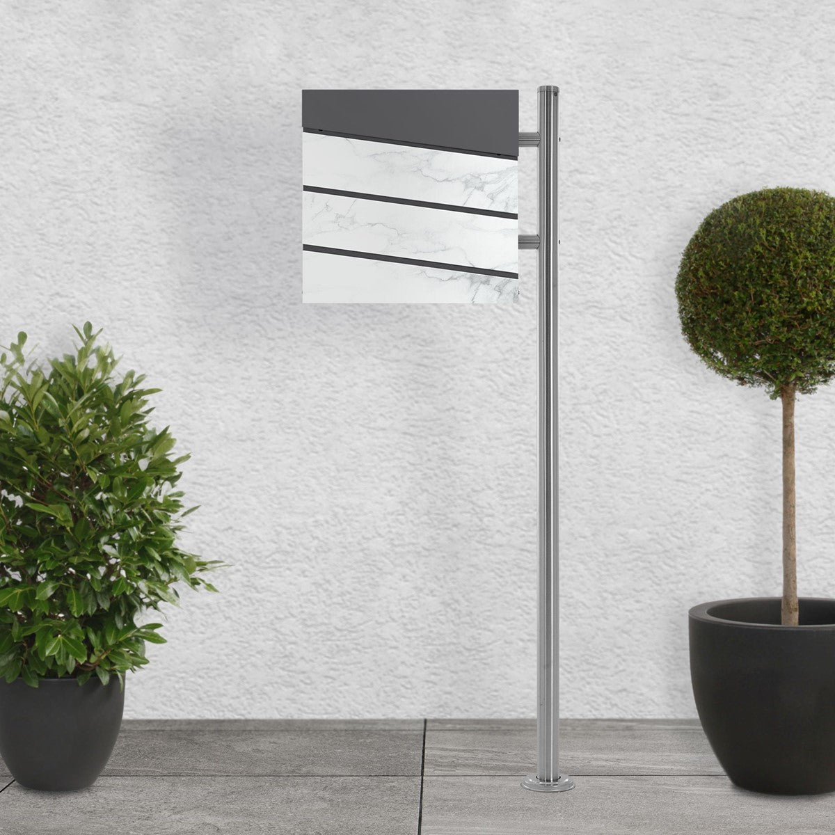 Briefkasten mit weißem Design und Pflanzen im Vordergrund.