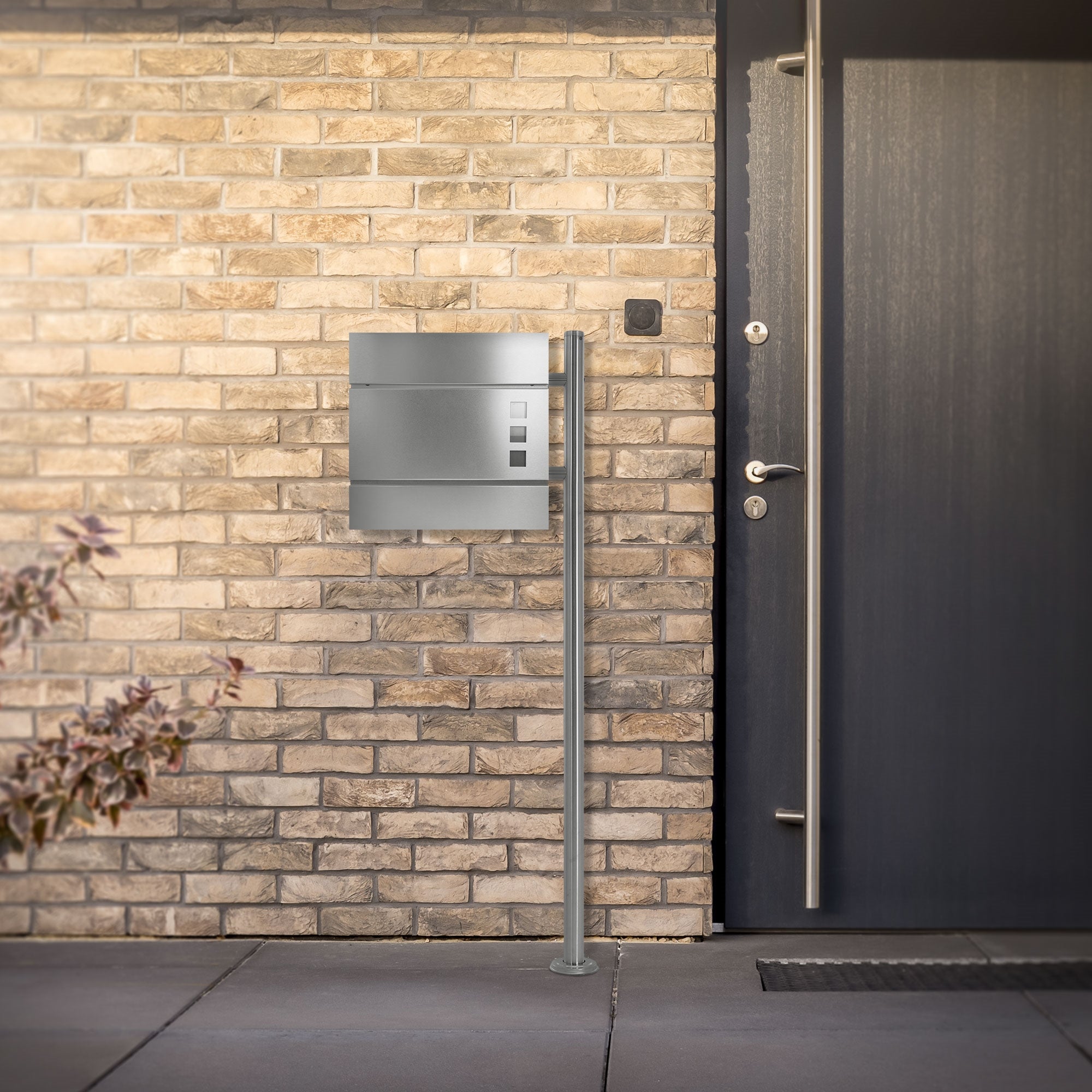 Stainless steel mailbox on a brick wall next to an entrance door.