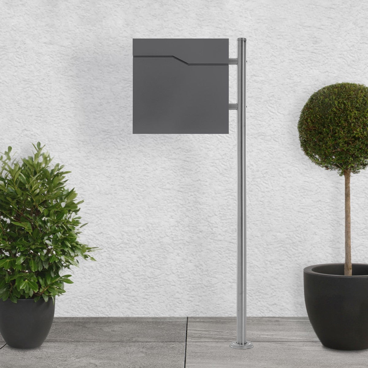 Gray mailbox on a stand, surrounded by two round potted plants.