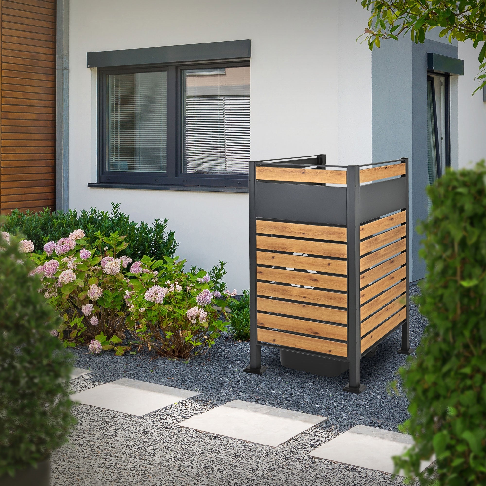 Holzoptik-Zaun mit Mülltonnen in einem Garten neben einem Haus.
