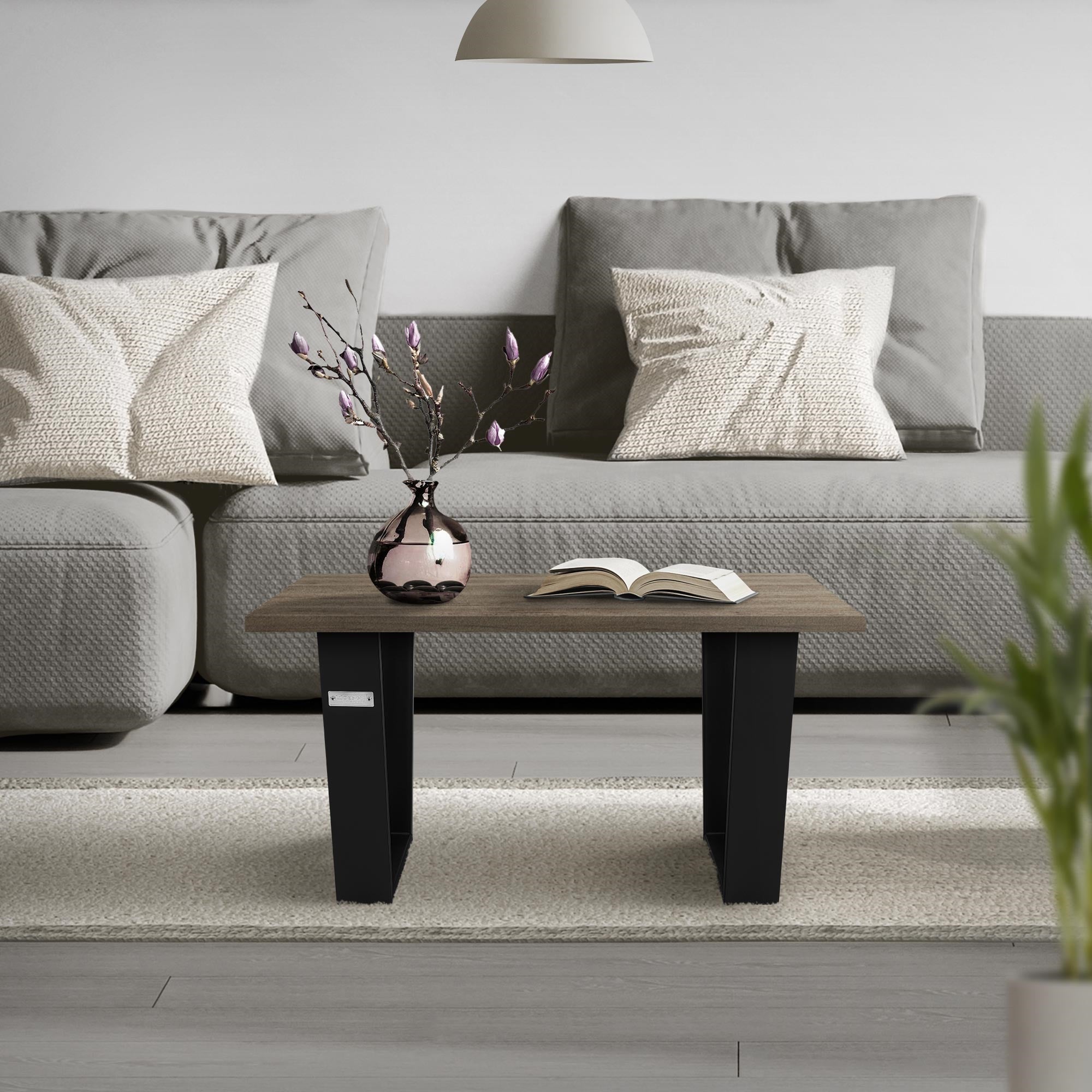 Kleiner Tisch mit Buch und Vase auf einem Teppich vor einem Sofa.