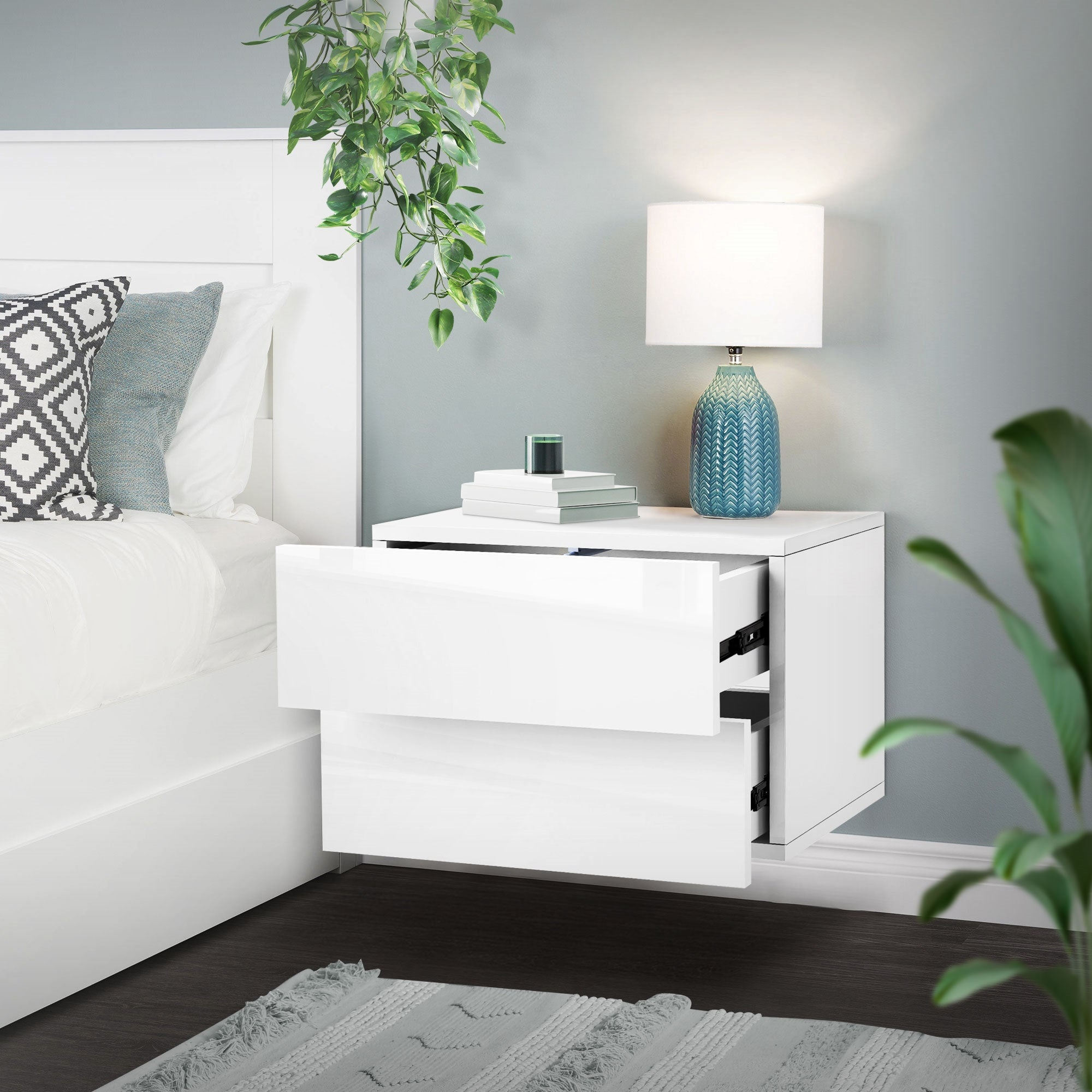 Nachttisch mit offenen Schubladen, Lampe und Pflanze.