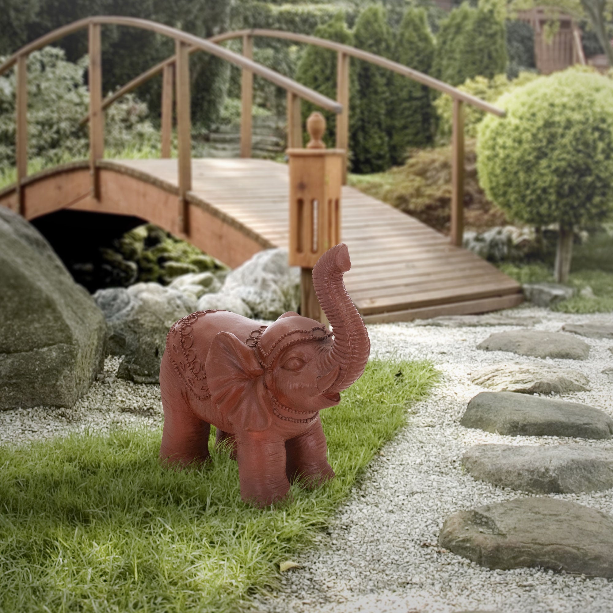 Elefante rosso in plastica nel giardino davanti a un ponte di legno.