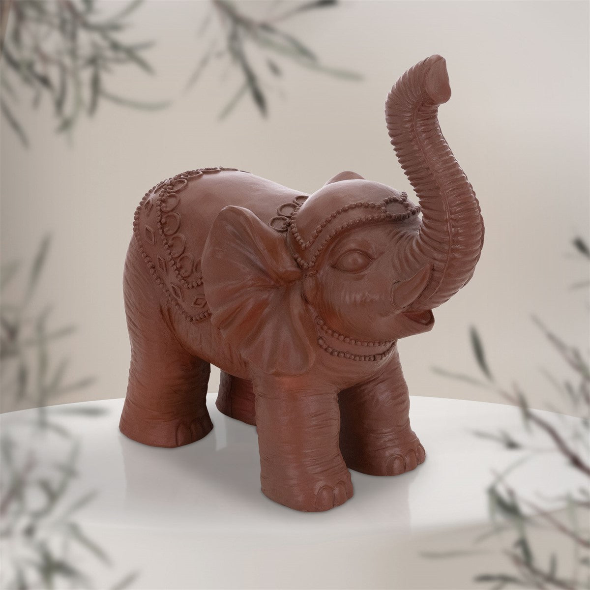 Brown elephant figurine on a white table with plants in the background.