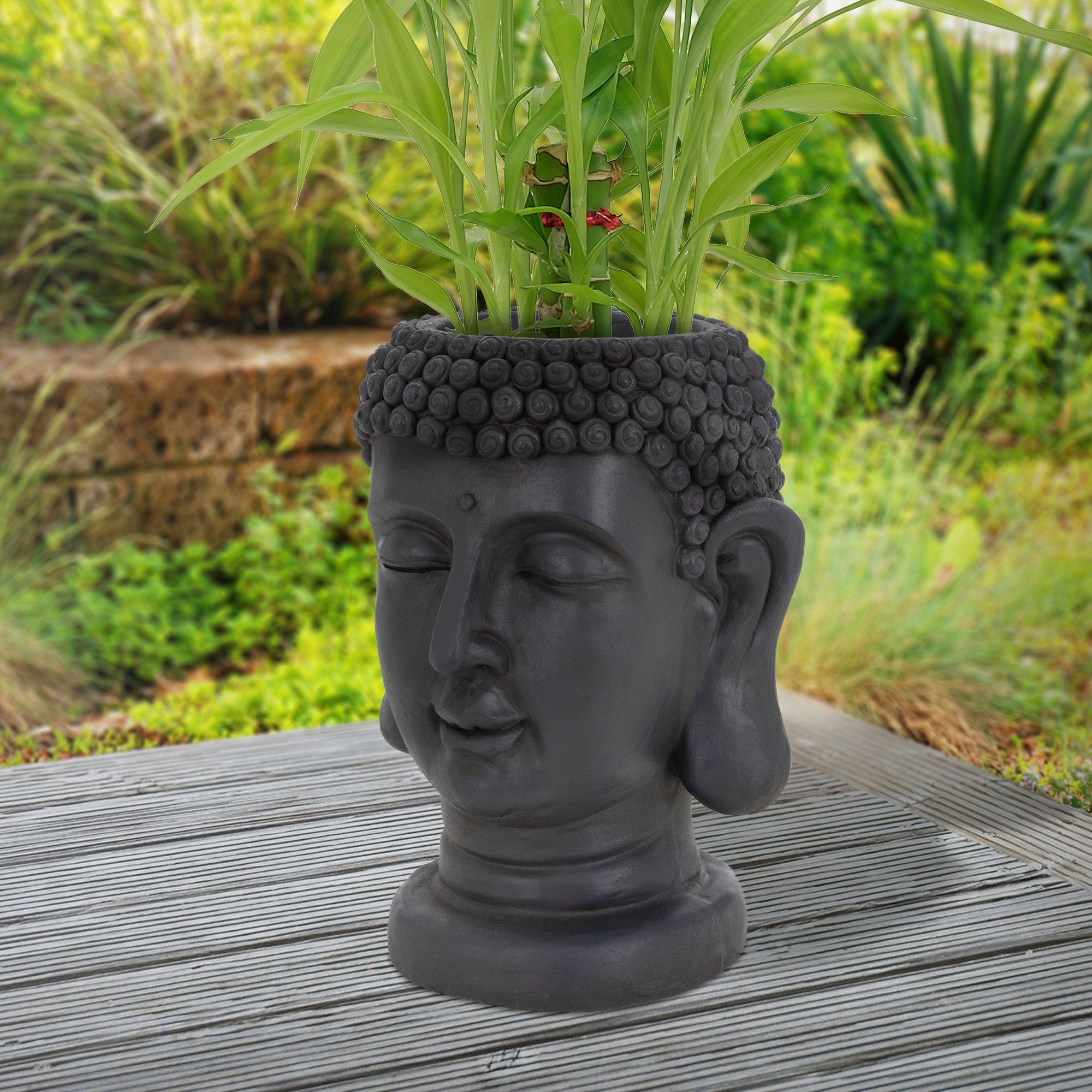 Buddha-Pflanztopf mit Pflanzen im Garten auf Holzuntergrund.