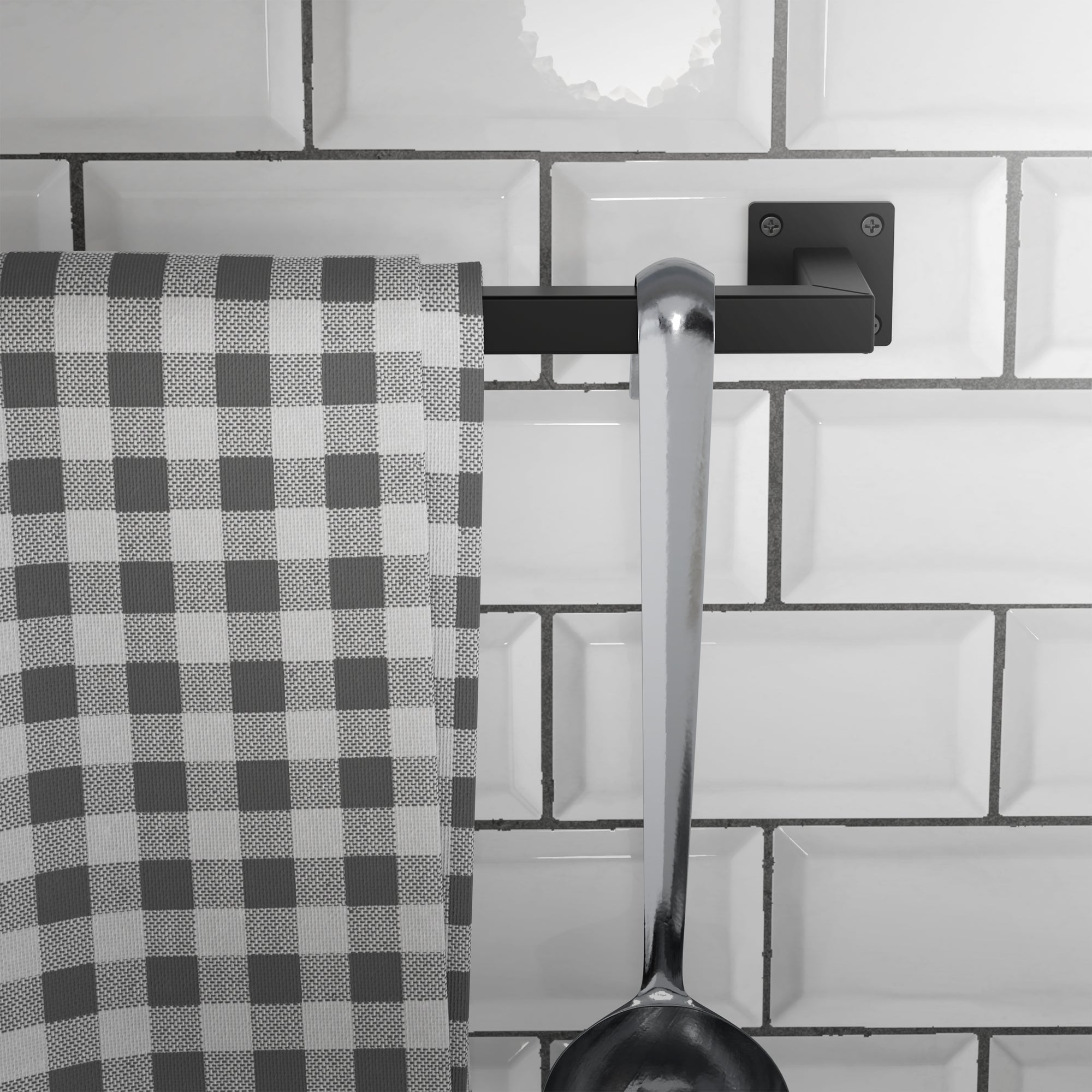 Kuchyňská utěrka a lžíce na černém držáku na dlaždicích.
