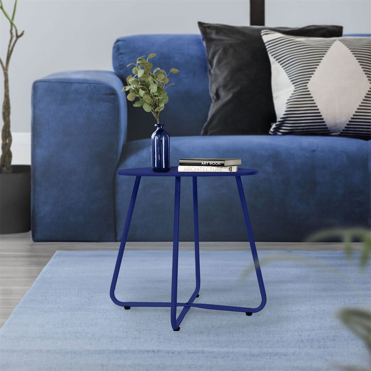 Sofá azul com almofadas e uma pequena mesa azul com um vaso e livros.