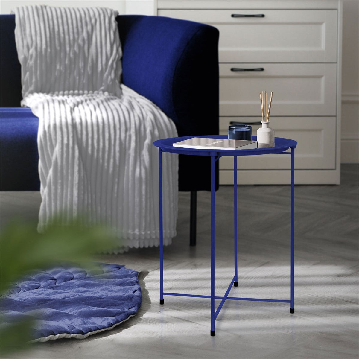 Ein blauer Beistelltisch mit einem weißen Tablett und einem schwarzen Behälter.