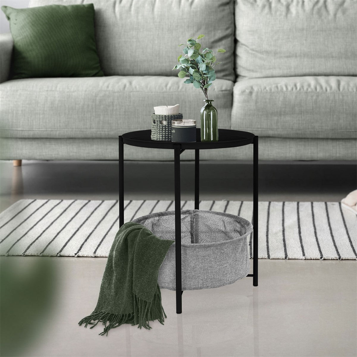 Black side table with decorations on a rug in front of a sofa.