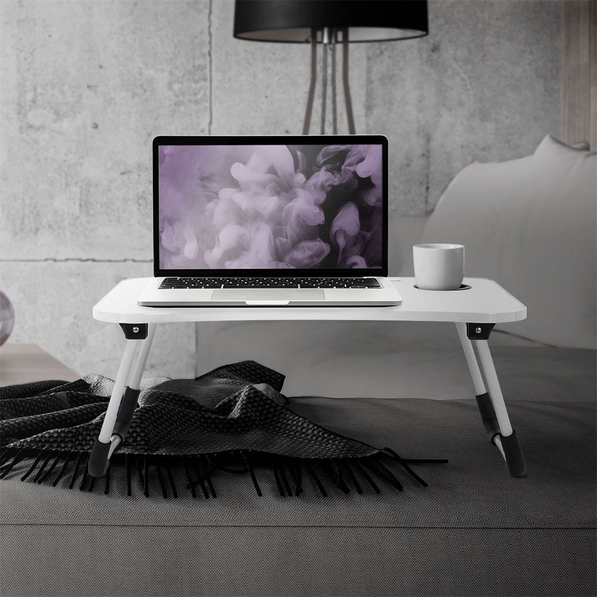 A laptop on a white folding table with a cup.