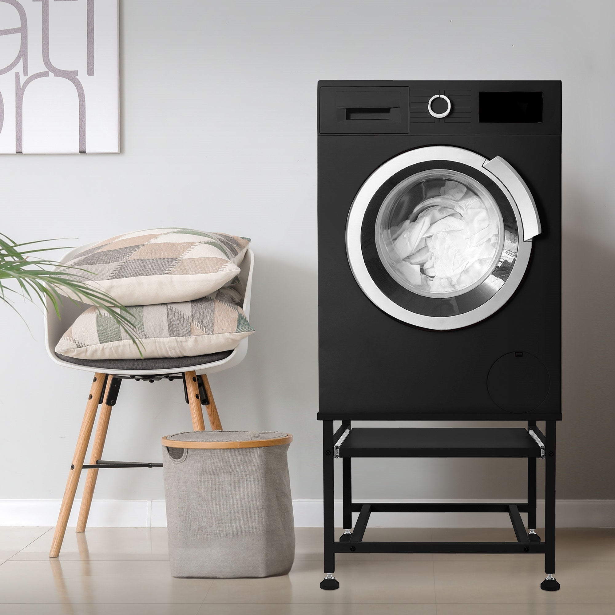 Machine à laver noire sur un support, à côté une chaise et un panier à linge.