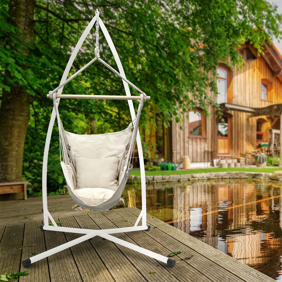 Hängesessel in beige mit Kissen, auf Holzdeck vor einem Haus und Wasser.