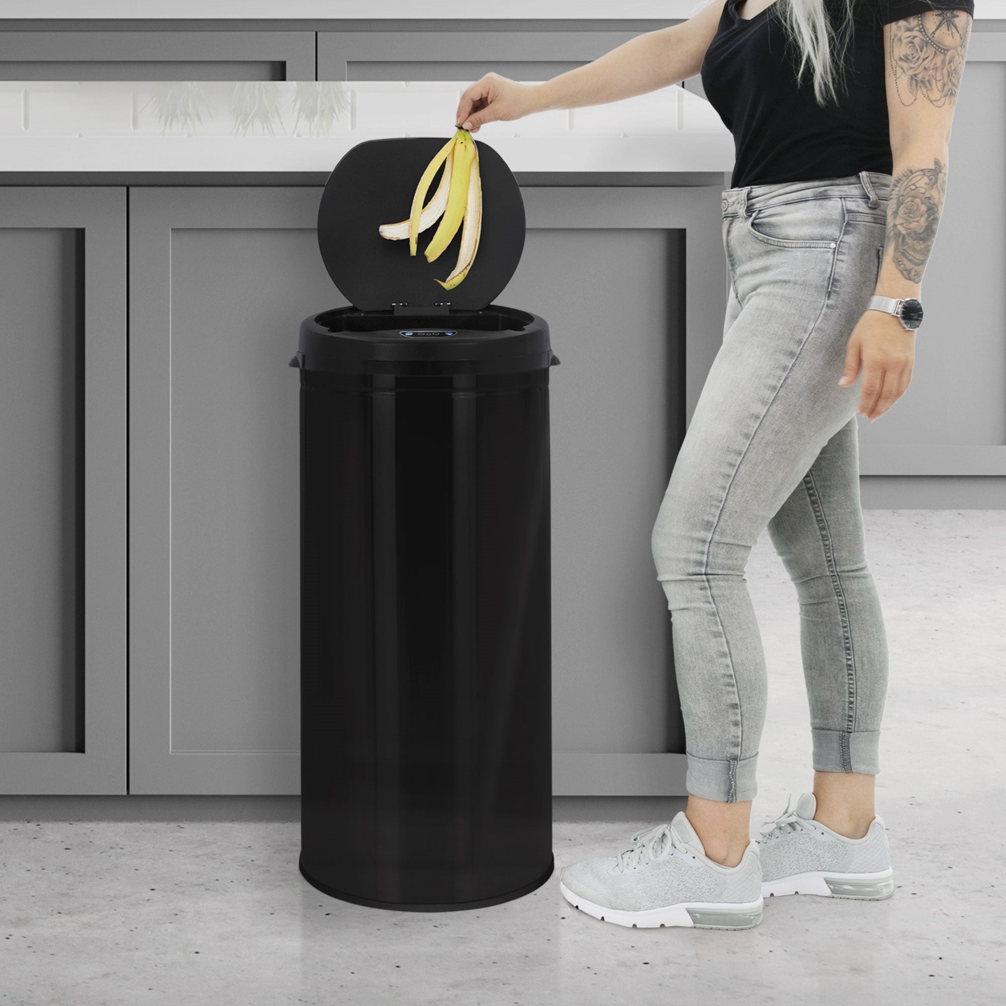 A person throws a banana into a black trash can in a modern kitchen.