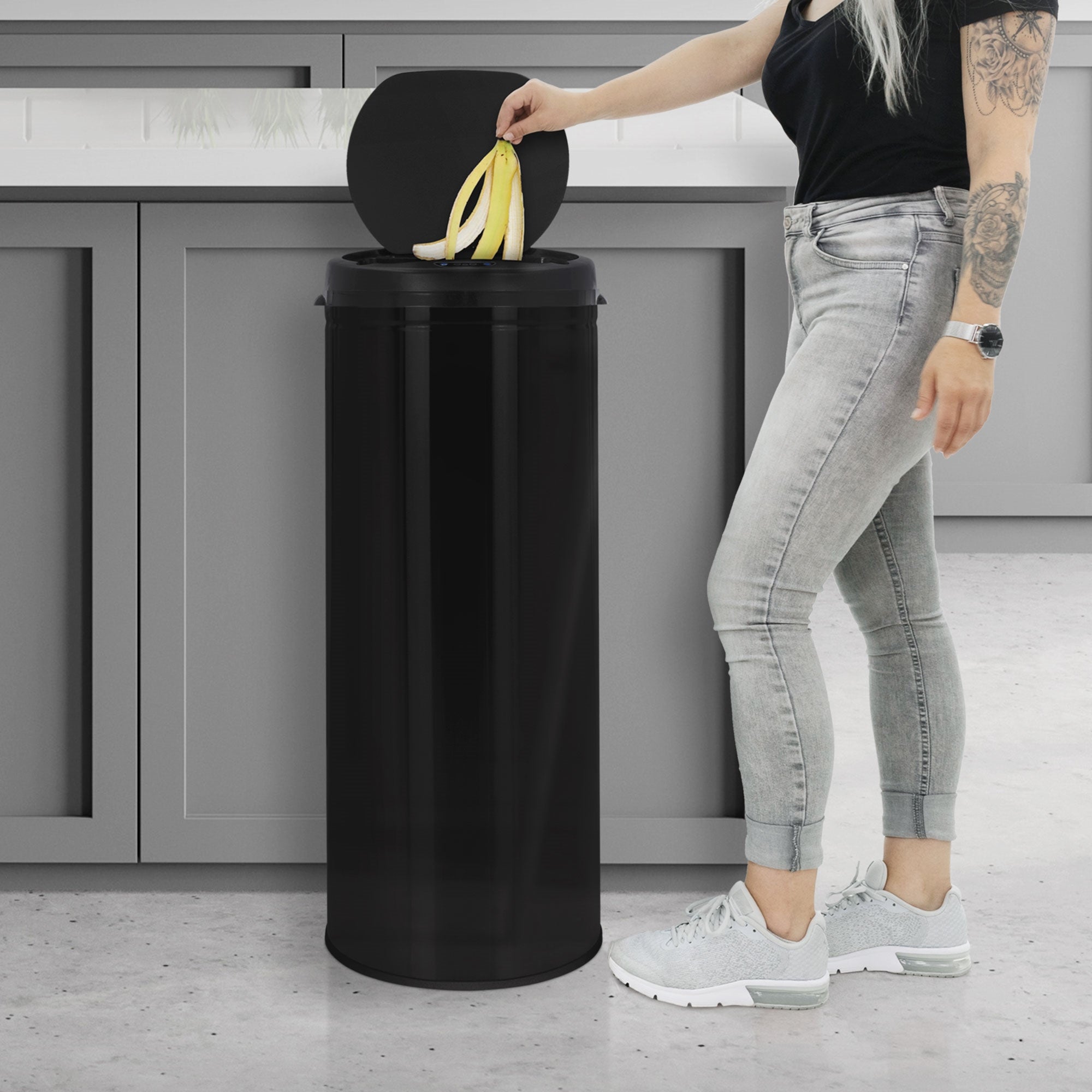 A person throws bananas into a black trash can in a modern kitchen.
