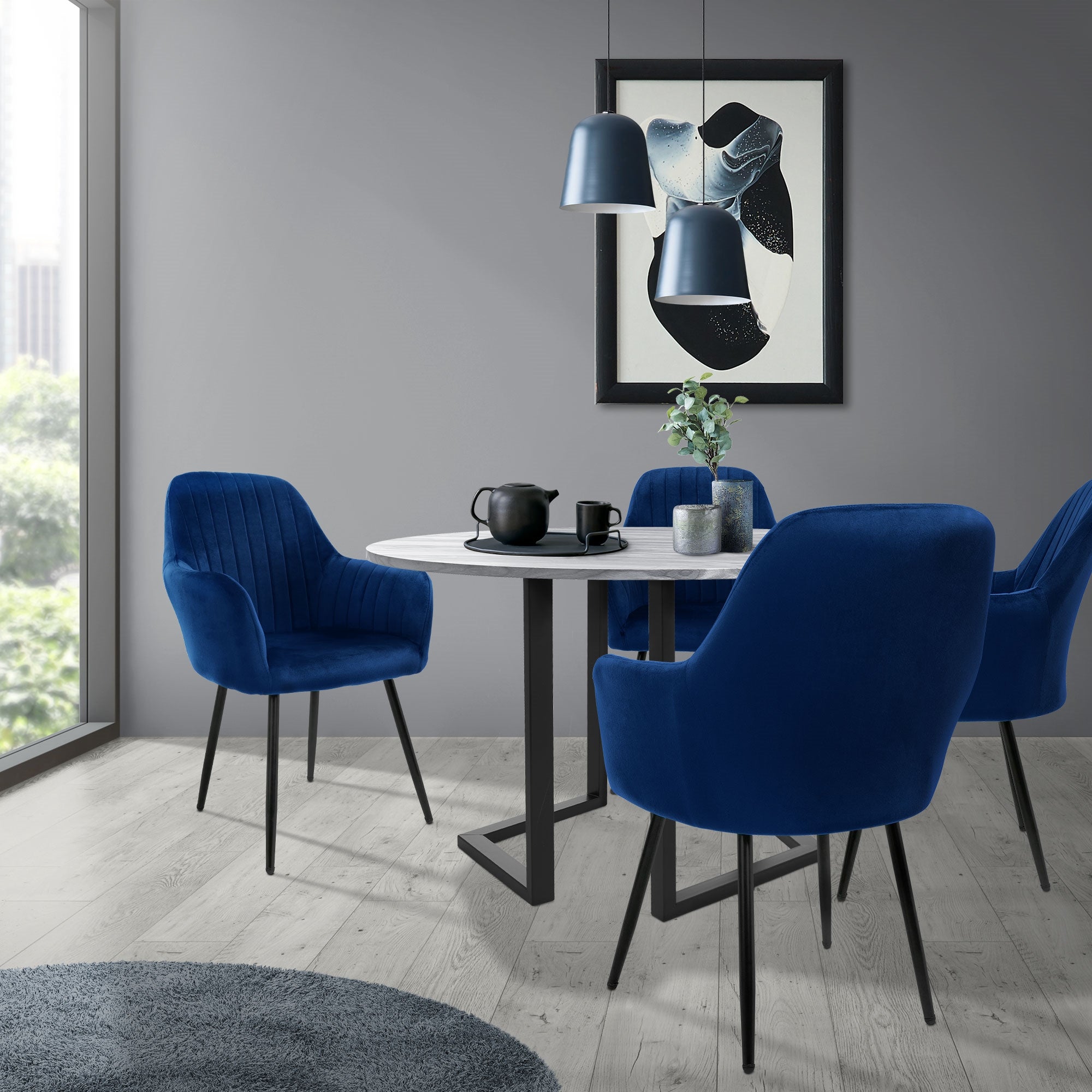 Zona pranzo con tavolo rotondo e quattro sedie blu davanti a una finestra.