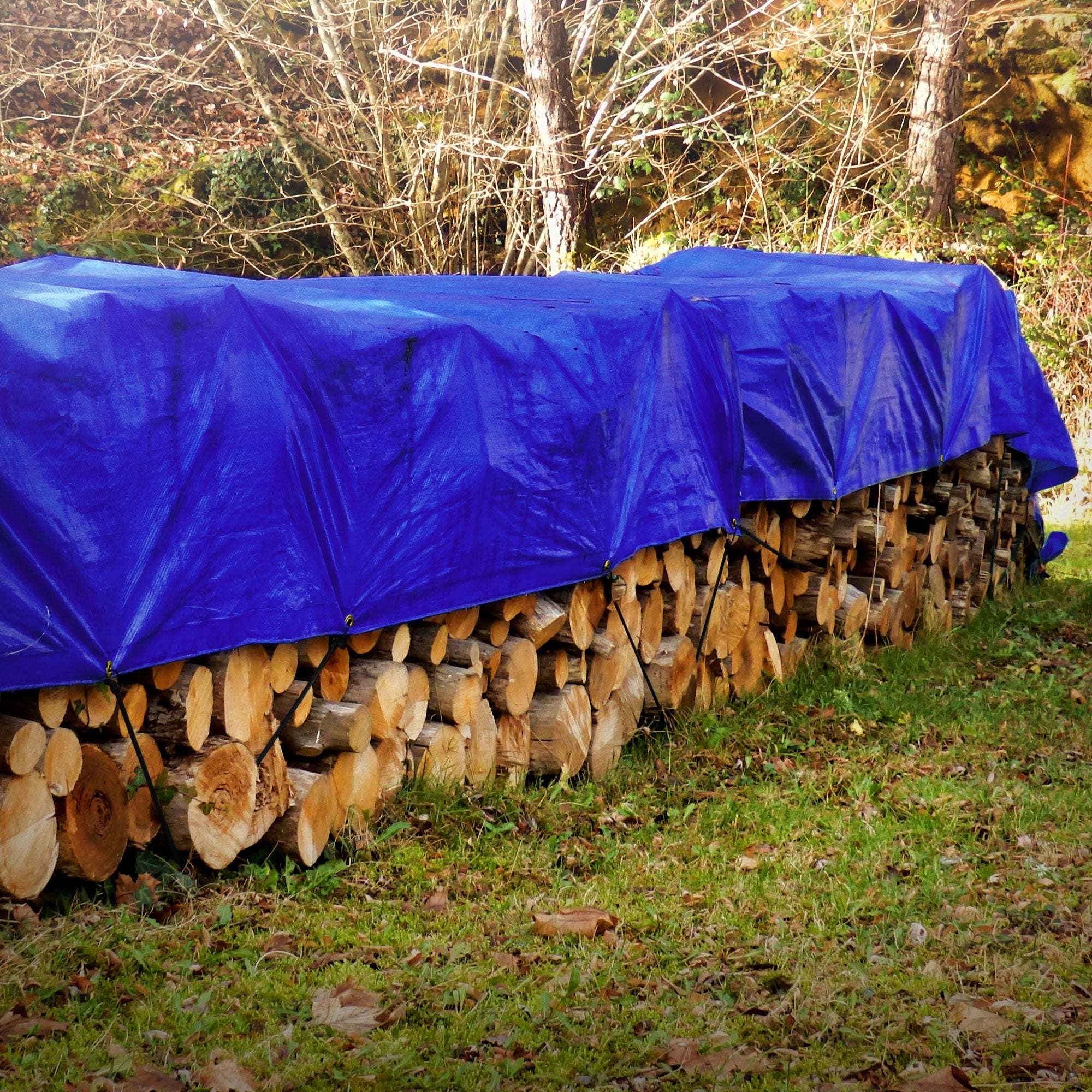 Blauer Planenstoff, der einen Holzstapel im Freien abdeckt.