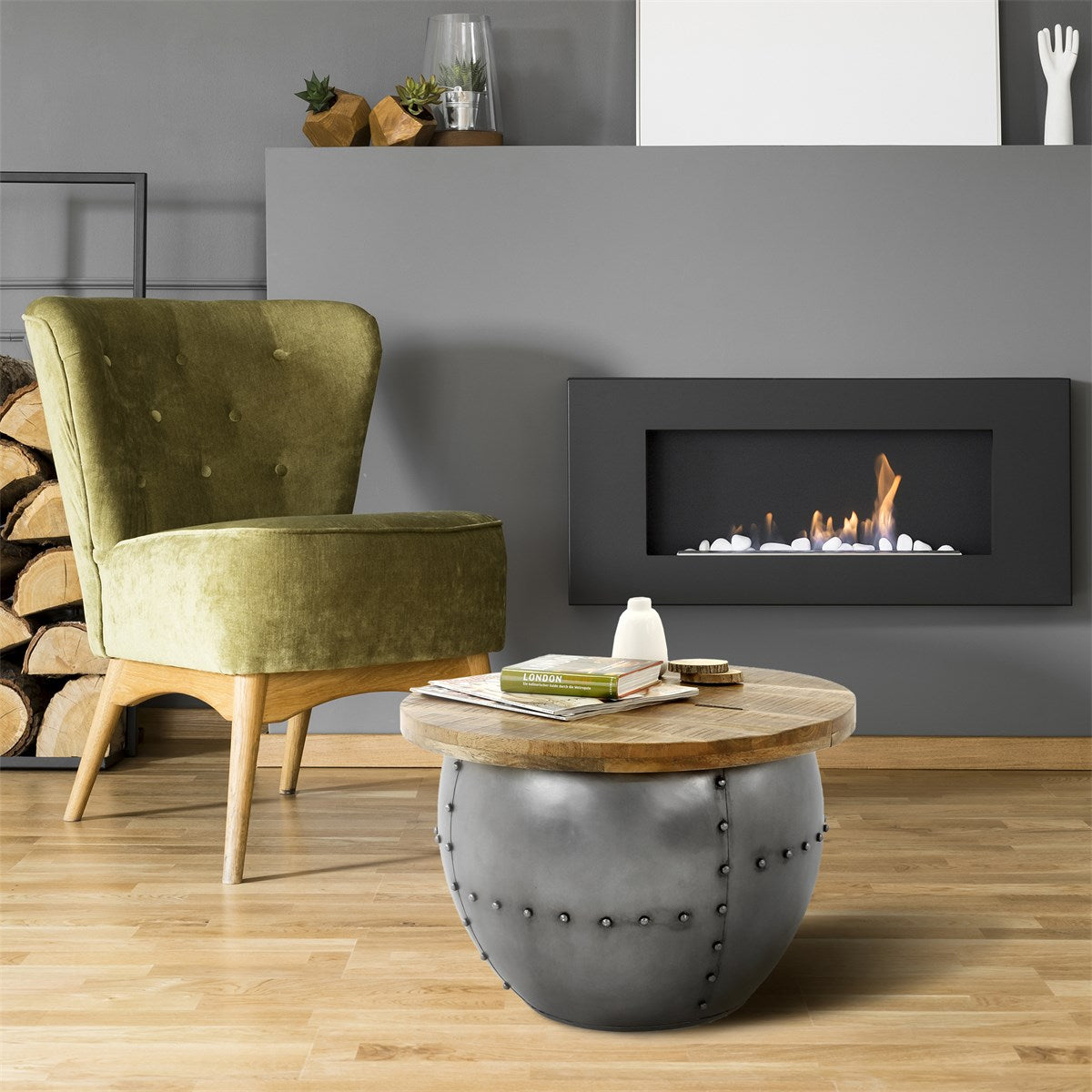 Green armchair next to a round wooden table and a modern fireplace in a living room.