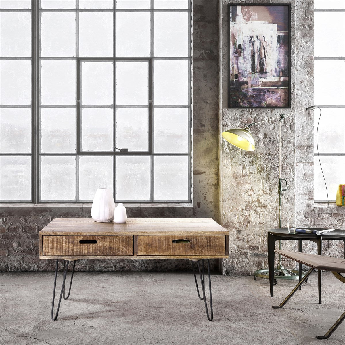 Wooden table with two drawers and metal legs in a room with large windows.