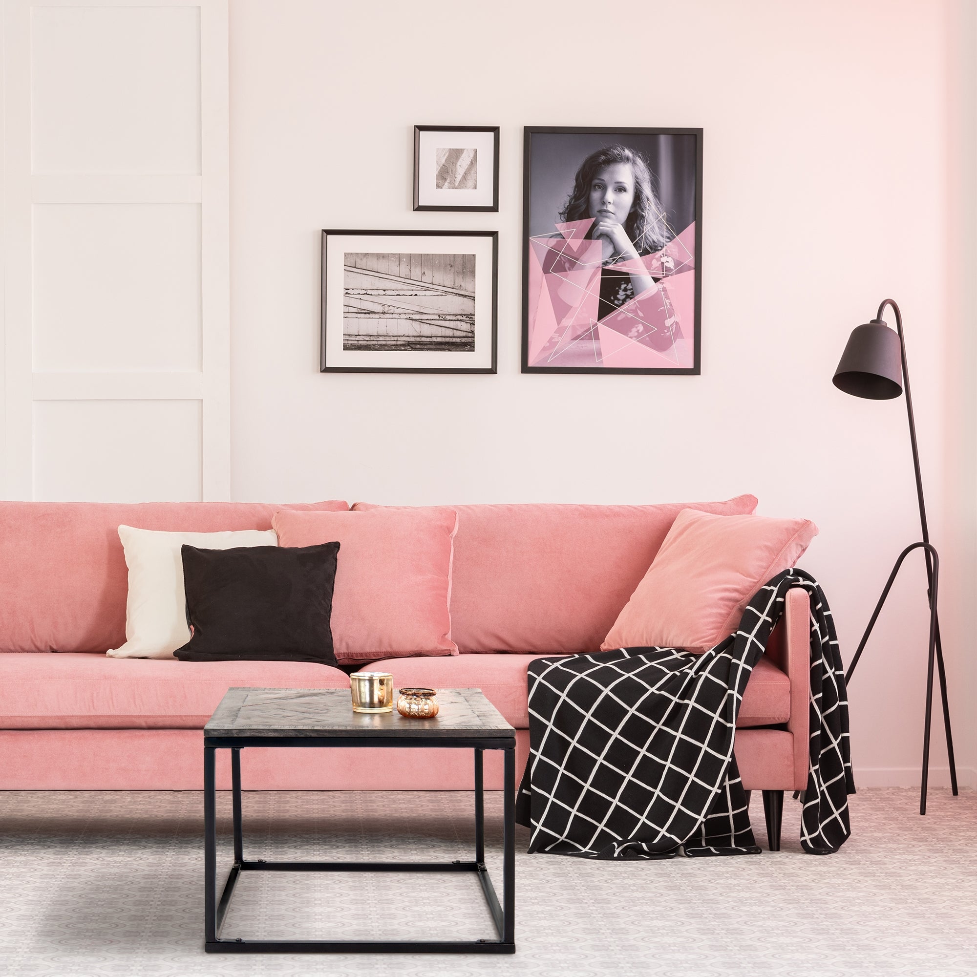 Rosa Sofa mit Kissen, schwarzem Überwurf und Tisch in einem hellen Raum.