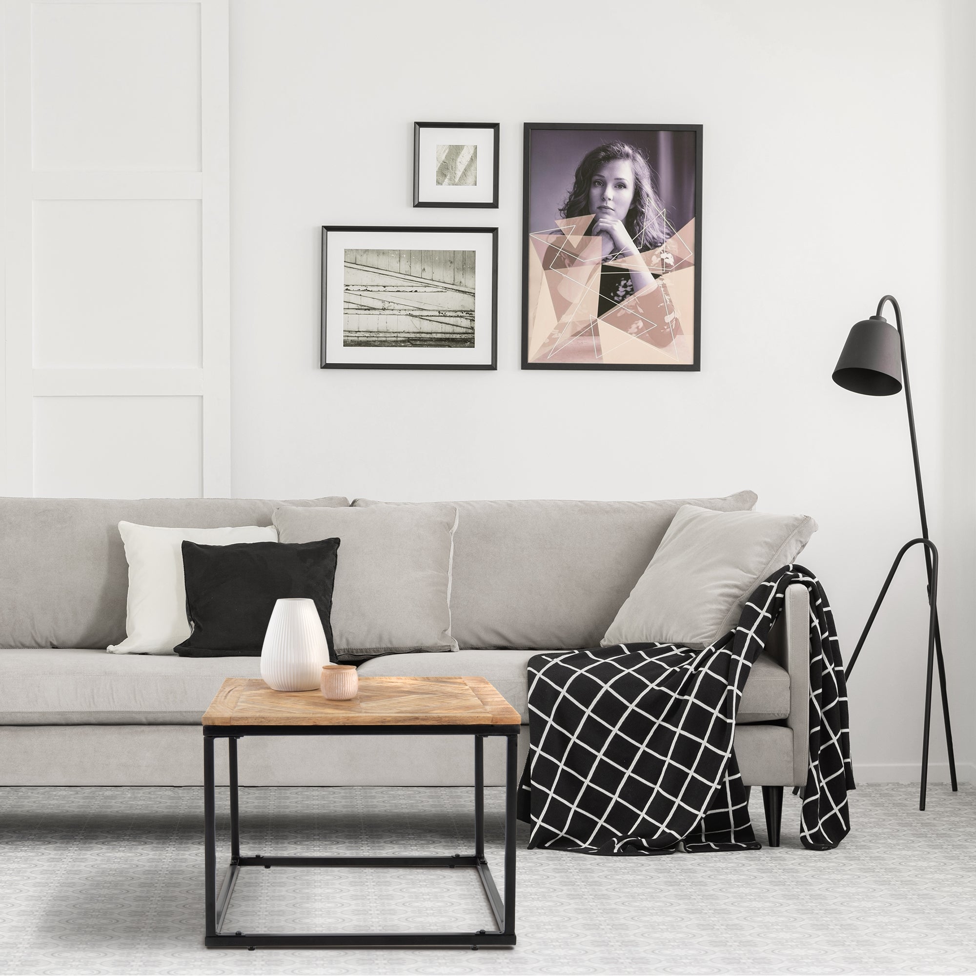 Een woonkamer met een grijze bank, kussens, tafel en schilderijen aan de muur.