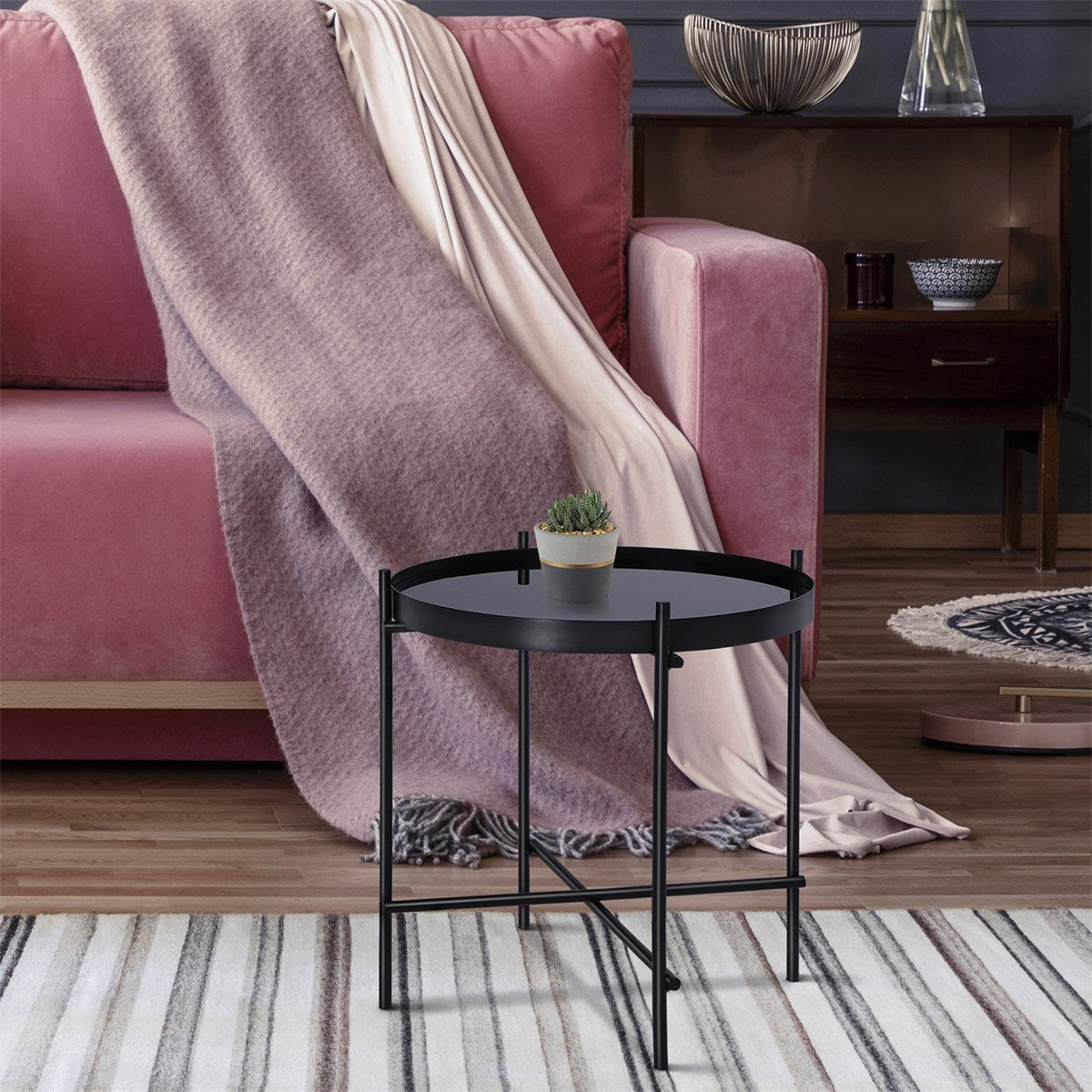 Schwarzer Beistelltisch neben einer rosa Couch, mit einer Pflanze auf der Tischplatte.
