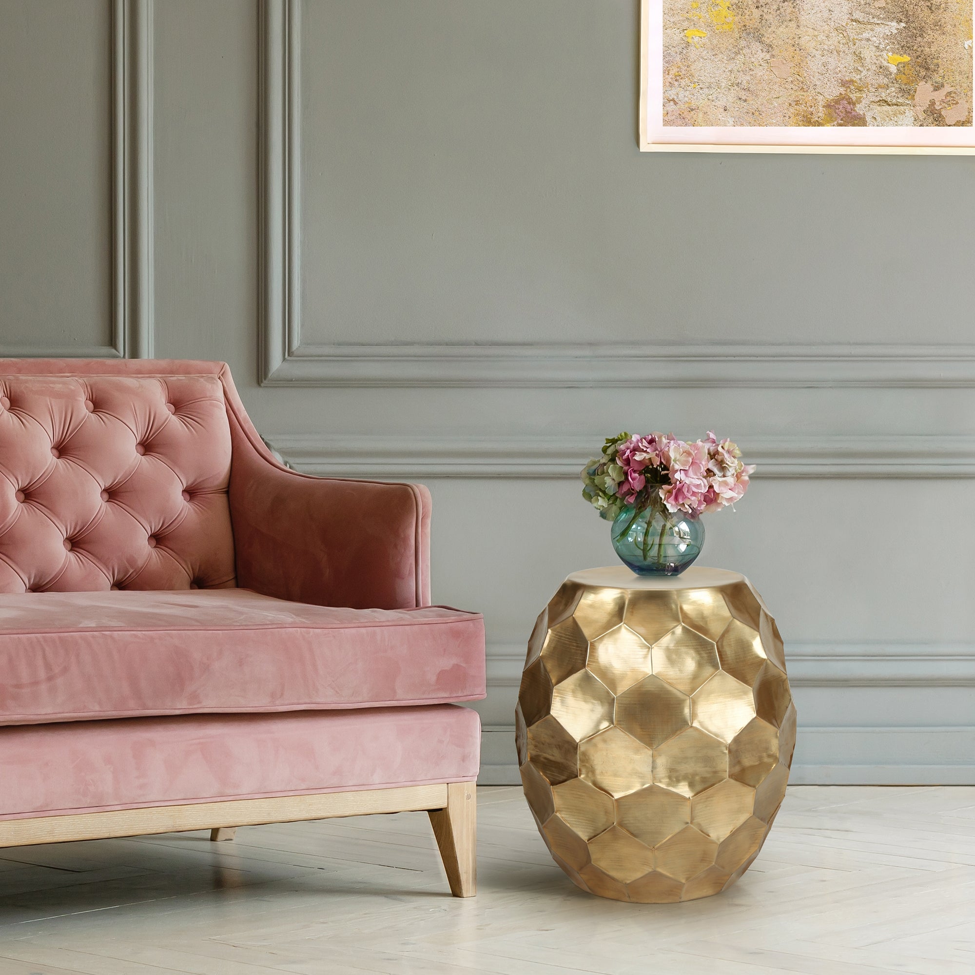 Divano rosa con tavolino dorato e fiori in una stanza elegante.