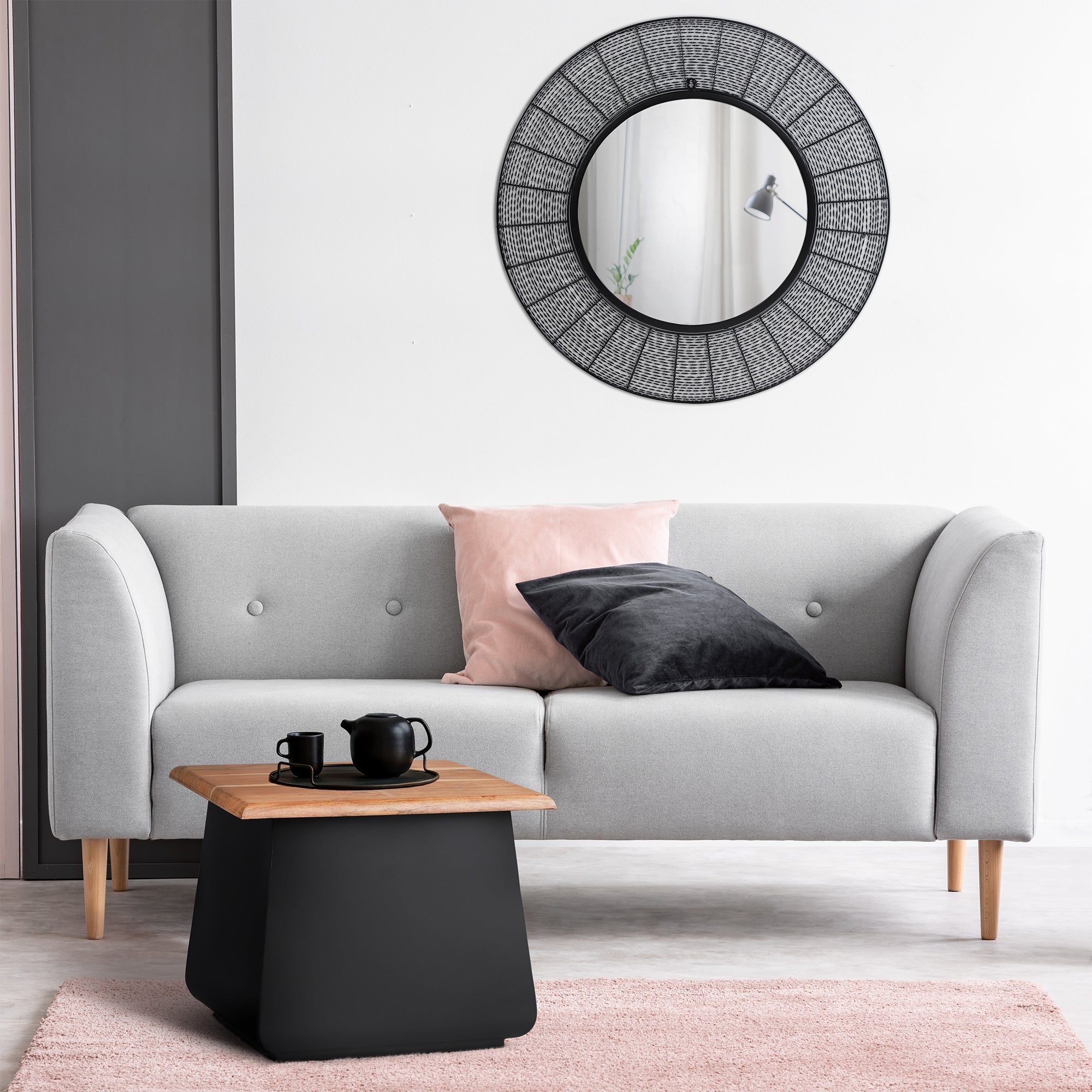 Ein graues Sofa mit Kissen, einem schwarzen Tisch und einem runden Spiegel.